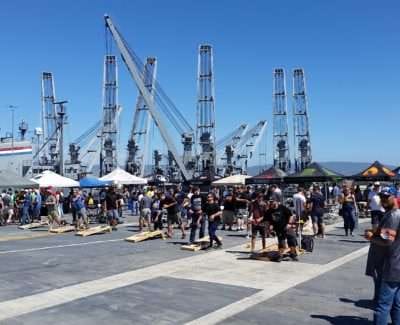 Crowds at USS Hornet event with industrial cranes in the background.