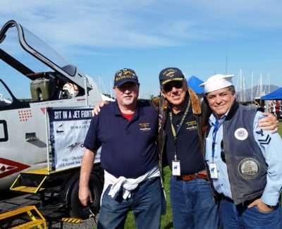 Veterans posing by jet fighter exhibit at USS Hornet event.