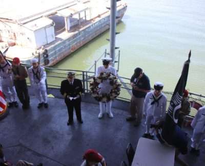 Naval officers holding a wreath during a ceremony on USS Hornet deck.