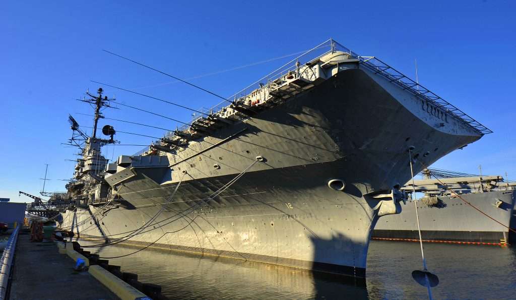 USS Hornet (CV-8), a large gray warship docked at a port.