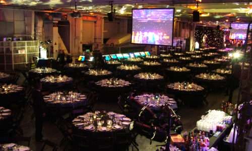 Formal dinner event with round tables, stage, and screen projections.