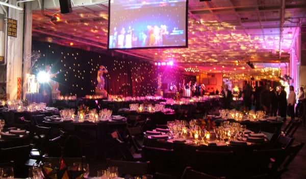 Elegant gala dinner setup with lights and stage inside large hall.