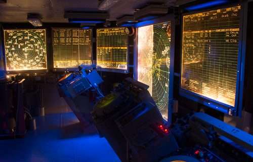 Ship bridge at night: radar screens, control panels, and navigation equipment.