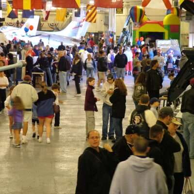 Crowd exploring aircraft and exhibits at an indoor aviation event.