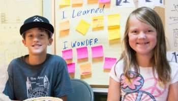 Smiling children sitting in front of learning board with sticky notes.