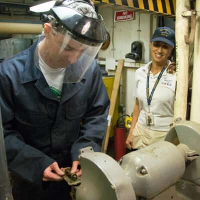 Worker in safety gear operating machinery while a someone observes.