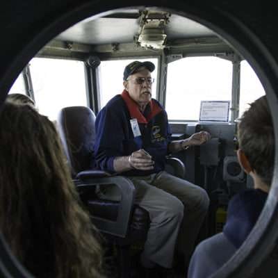 Tour guide explaining ship controls to visitors in a vessel's control room.