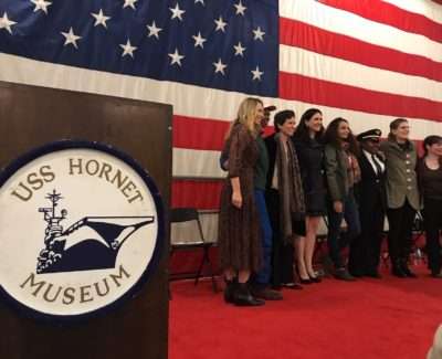 Group posing at USS Hornet Museum in front of American flag.