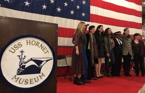 Group posing at USS Hornet Museum in front of American flag.