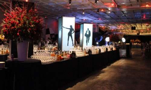 Elegant bar setup with illuminated posters and flowers at event.