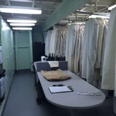 Laundry room with white uniforms hanging and a table with clipboard and laundry items.