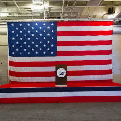 Podium with USS Hornet Museum logo in front of large American flag.