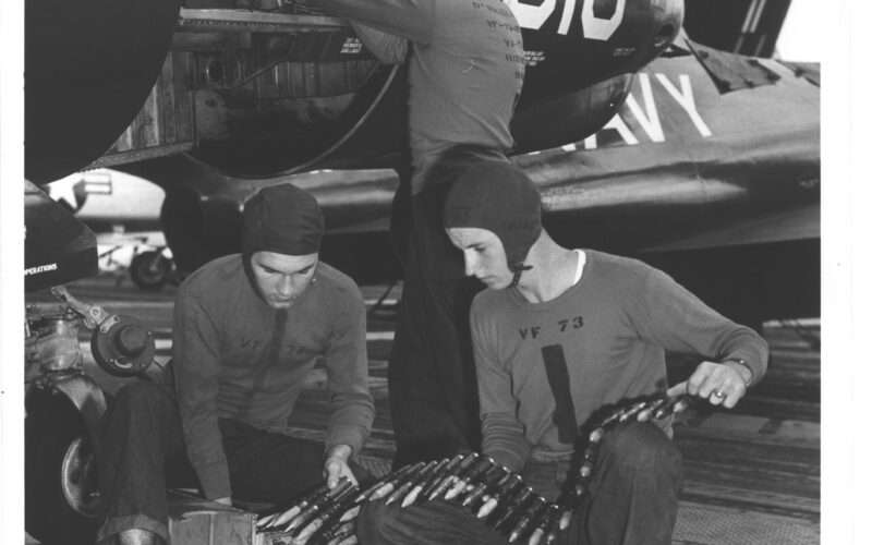 Navy personnel loading ammunition into aircraft on USS Hornet, black and white photo.