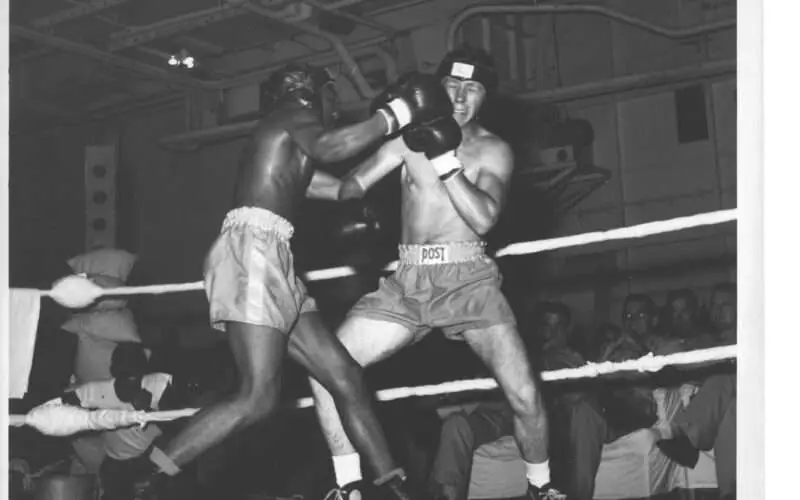 Boxing match between two men on USS Hornet, spectators watching, black and white photo.