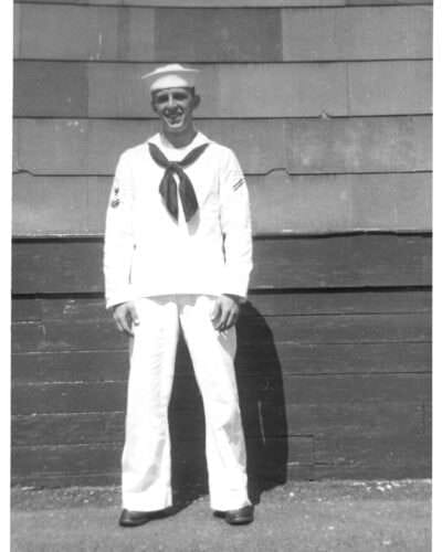 Navy sailor in white uniform standing against a wall, black and white photo.