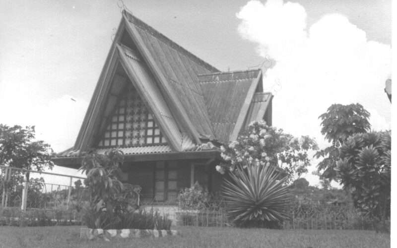 Traditional thatched roof house with lush garden, black and white photo.