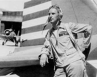 Captain Diz Laird in aviator gear leaning on aircraft with another plane in the background.