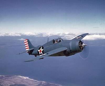 WWII Grumman F4F Wildcat fighter aircraft flying over the ocean.