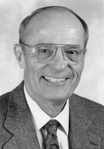 Donald Jones in a suit and tie, wearing glasses, smiling in a portrait.