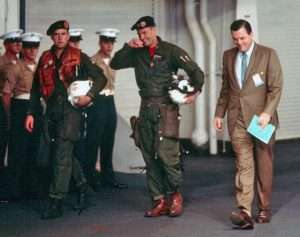 Helicopter crew in flight suits and berets walking aboard USS Hornet.