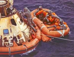 Apollo 11 astronauts in life raft being retrieved by recovery crew.