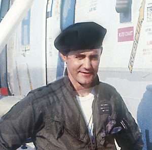 Milt Putnam in flight suit and beret standing beside a helicopter.