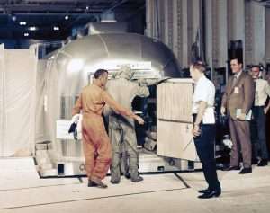 Quarantine capsule Hornet + 3 being inspected by men in protective suits on USS Hornet hangar deck